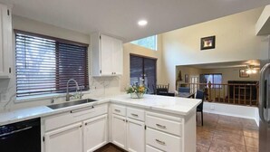 A kitchen with white cabinets, a sink, and a dining area with a table and chairs.
