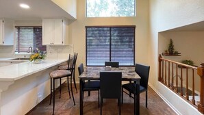 A compact kitchen with a dining area, featuring a marble countertop, a dining table with chairs, and a window with blinds.