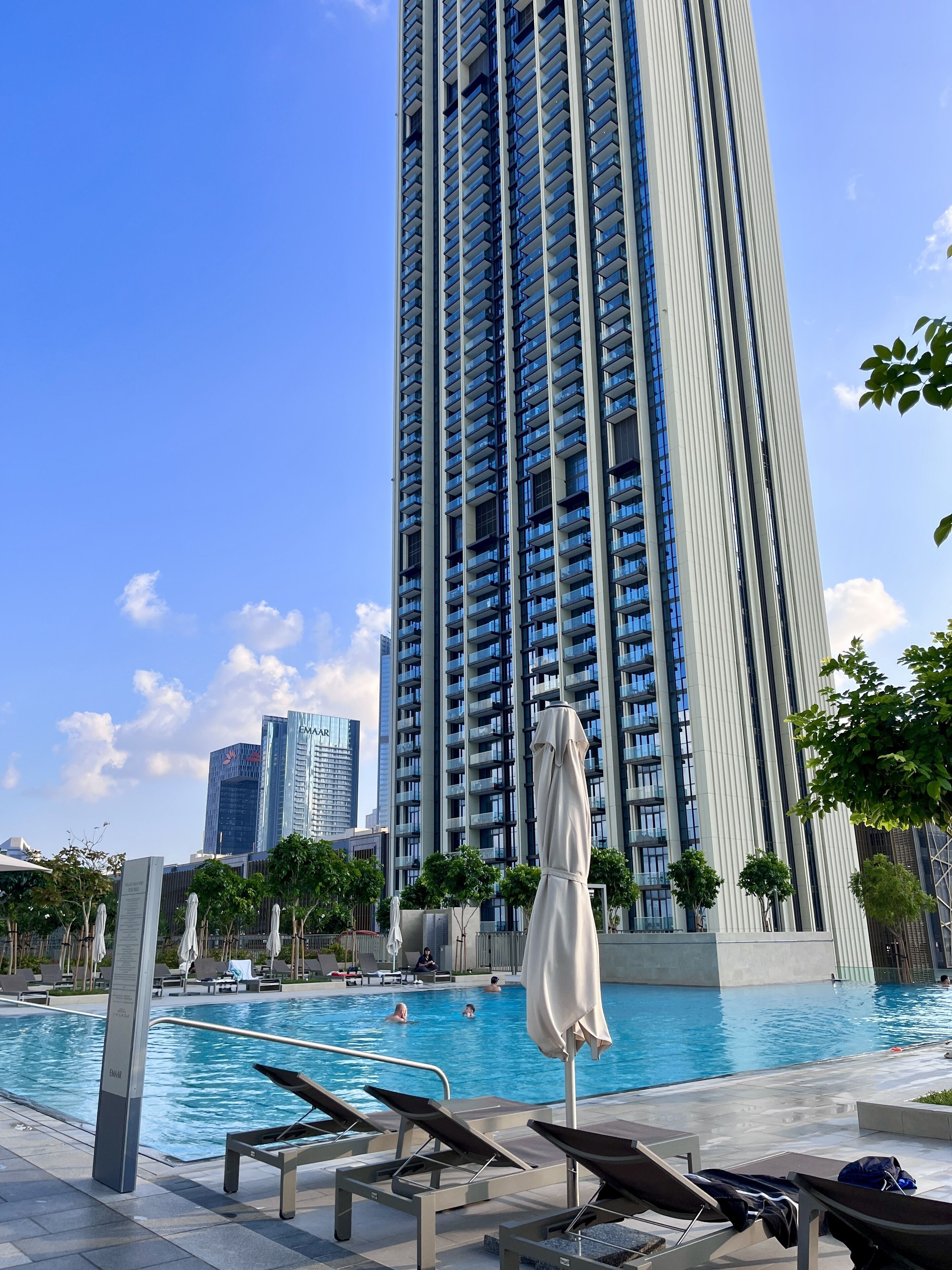 A high-rise building with a swimming pool, lounge chairs, and umbrellas.