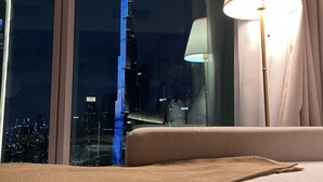 Une chambre d’hôtel dotée d’une grande fenêtre donnant sur le panorama urbain, avec notamment un gratte-ciel imposant.