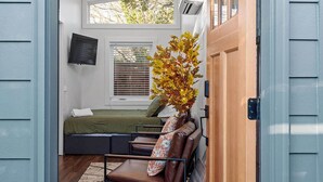 A cozy room with a bed, a seating area, and a window with blinds. - Chic Downtown Raleigh Tiny House (Raleigh)
