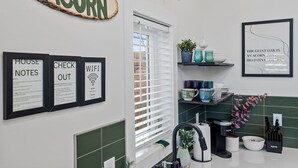 A modern kitchen with a green and white color scheme, a sign reading "THE ACORN", and framed notices for "HOUSE NOTES", "CHECK OUT", and "WIFI". - Chic Downtown Raleigh Tiny House (Raleigh)