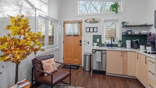 A modern kitchen with wooden cabinets, a stainless steel sink, and a window with a view of trees. - Chic Downtown Raleigh Tiny House (Raleigh)