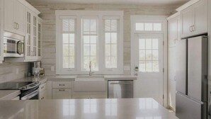 A modern kitchen with white cabinetry, a stainless steel refrigerator, and a built-in oven. - The Sundance Cottage (Wrightsville Beach)