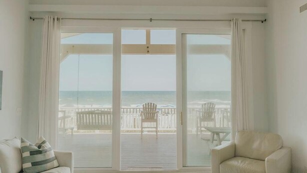 A room with a large sliding glass door leading to a balcony overlooking the ocean. - The Sundance Cottage (Wrightsville Beach)