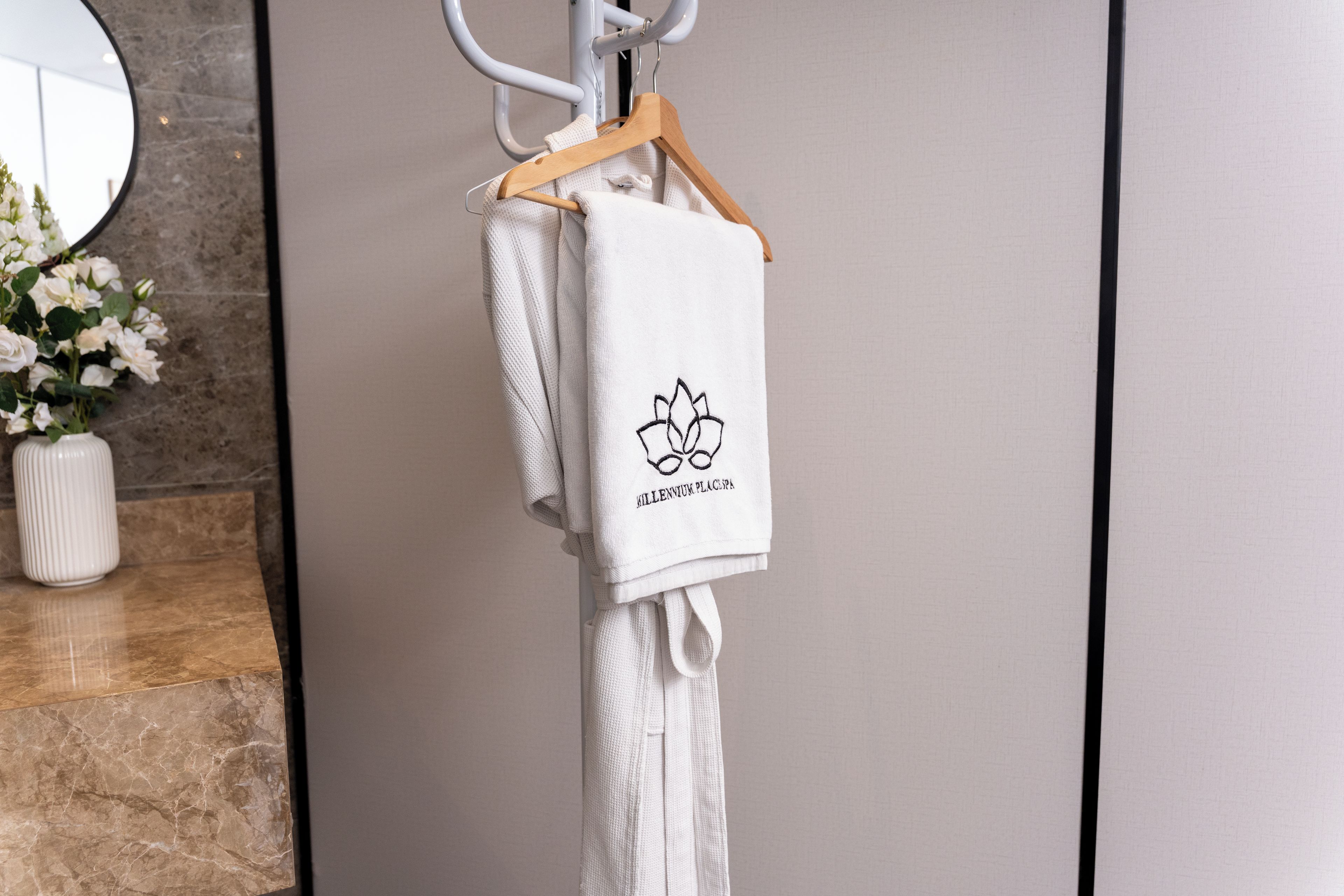 Ein weißes Handtuch mit einem Logo und Schriftzug hängt an einem Holzgalgen in einem Badezimmer.