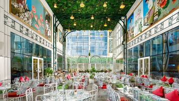 A restaurant with glass tables and chairs, a green ceiling, and murals on the walls.