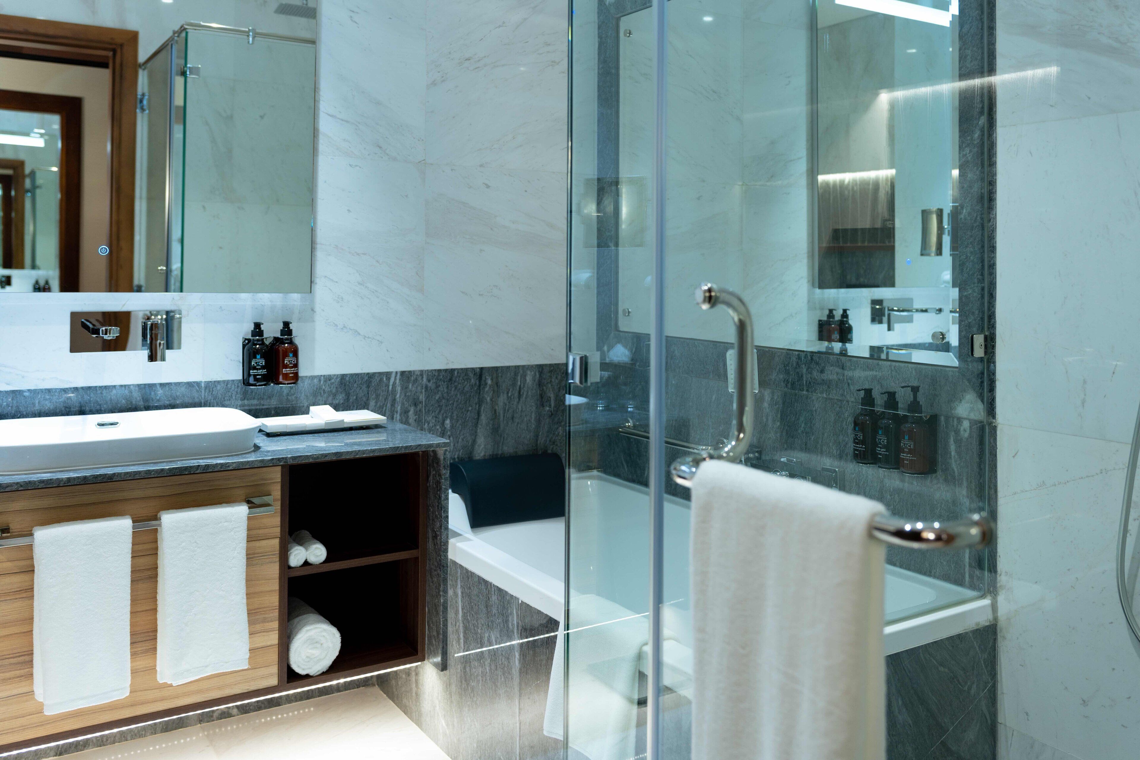 Une salle de bain moderne avec une douche à parois de verre, un meuble-lavabo en marbre et un grand miroir.