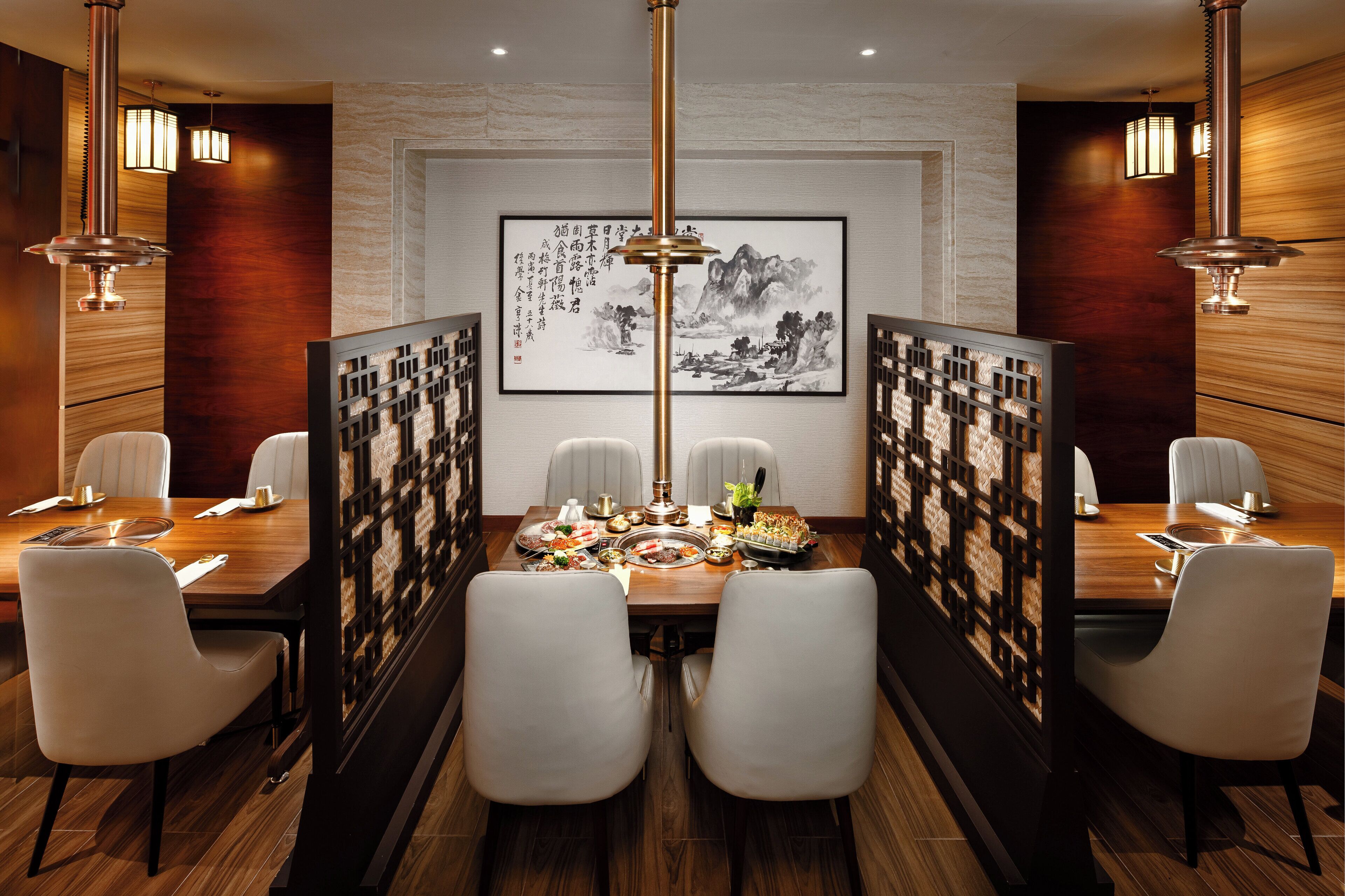 A dining area with a wooden table set for two, surrounded by white chairs, with a traditional Chinese painting on the wall and a decorative screen in the background.