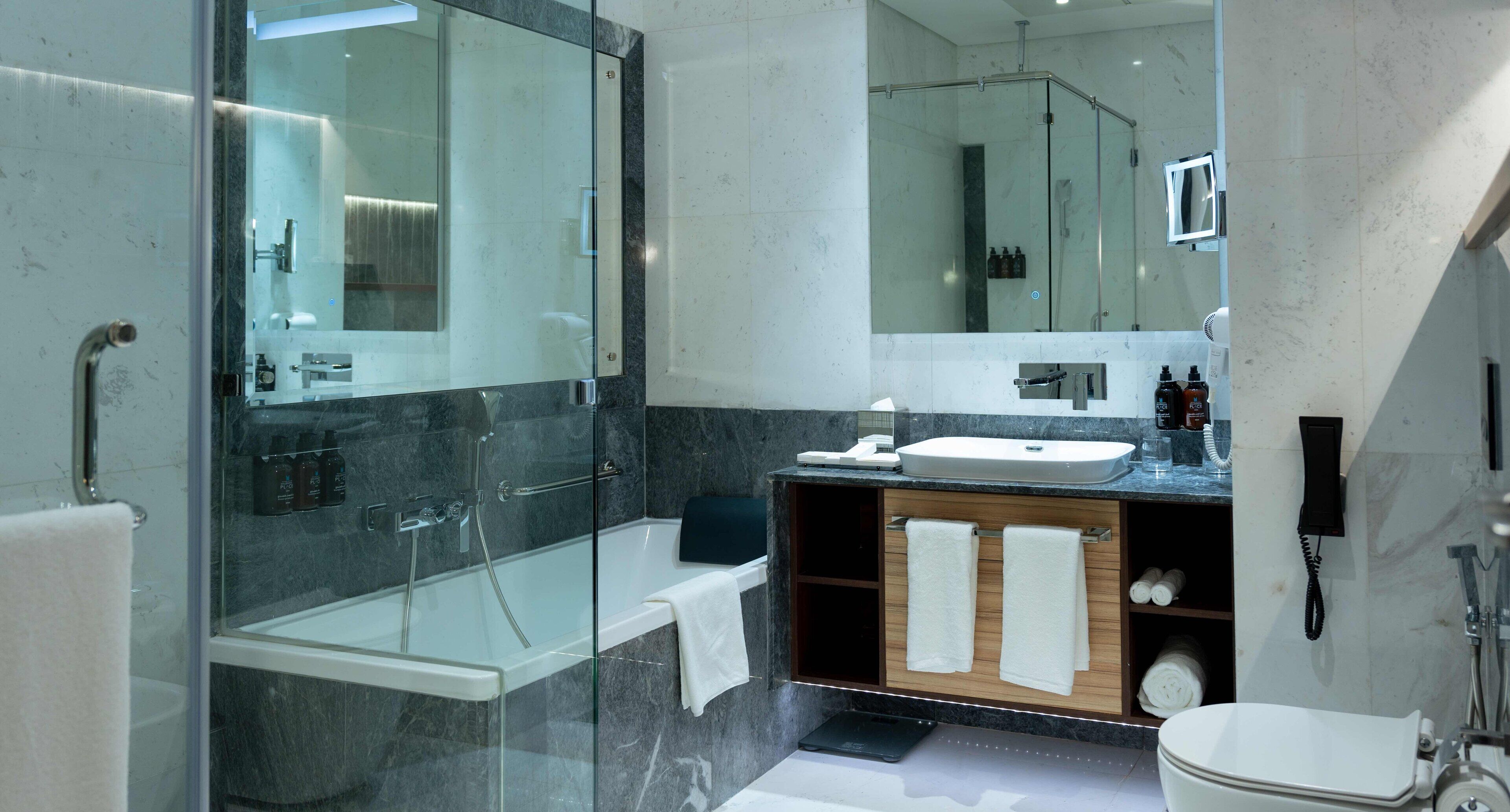 A modern bathroom with a glass-enclosed shower, a white bathtub, a vanity with a sink, and a toilet.