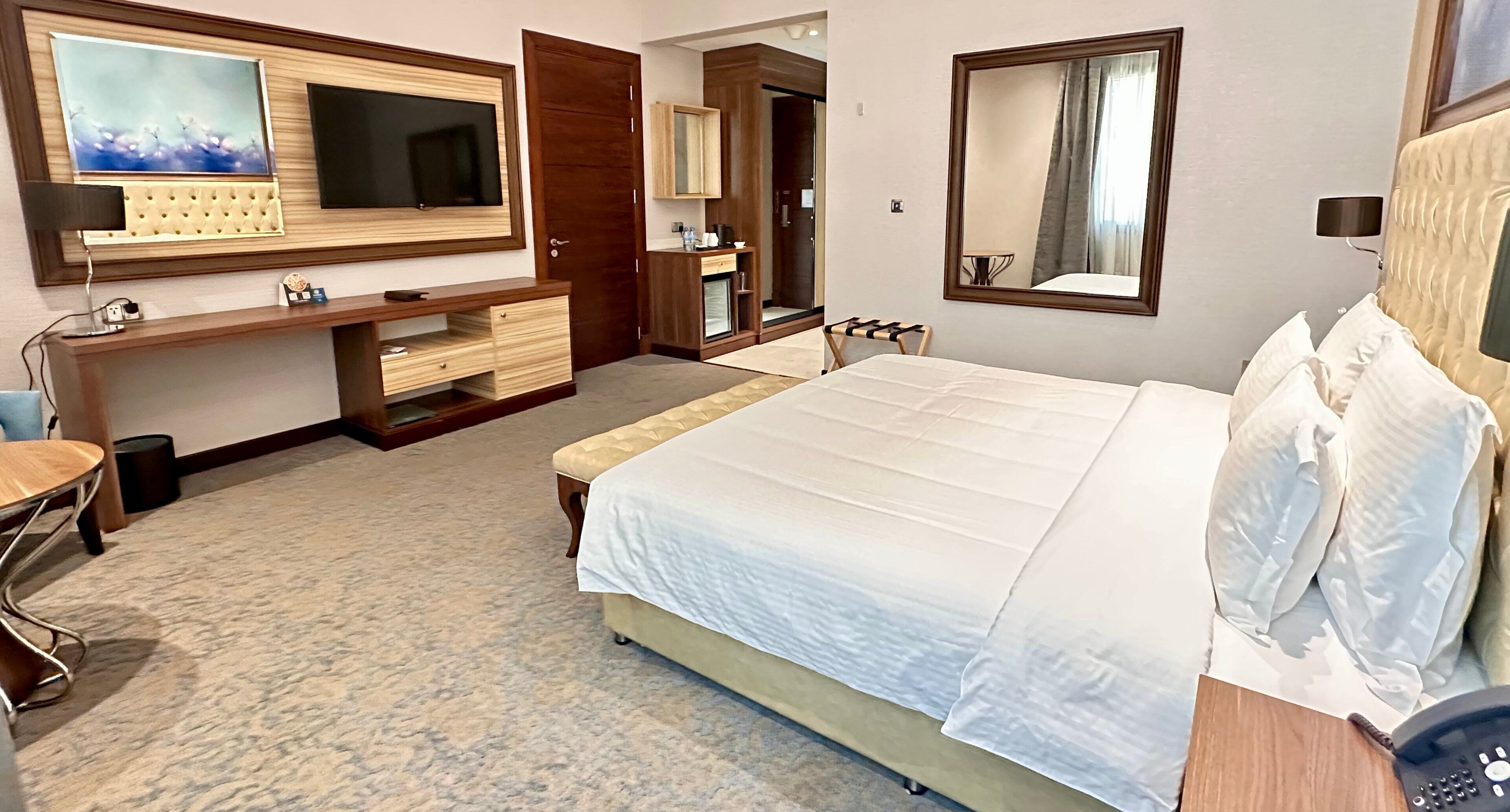 Ein Hotelzimmer mit einem großen Bett, einem Fernseher, einem Schreibtisch mit Stuhl, einem Schminktisch und einem Spiegel.