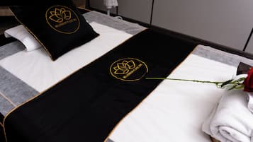 Una cama bien hecha con una colcha blanco y negro, dos almohadas con un logotipo y una sola rosa.