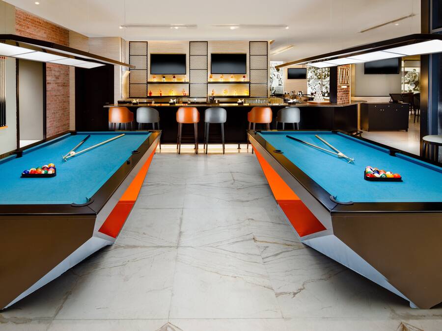 A pool table area with two tables, bar stools, and a bar with a TV.