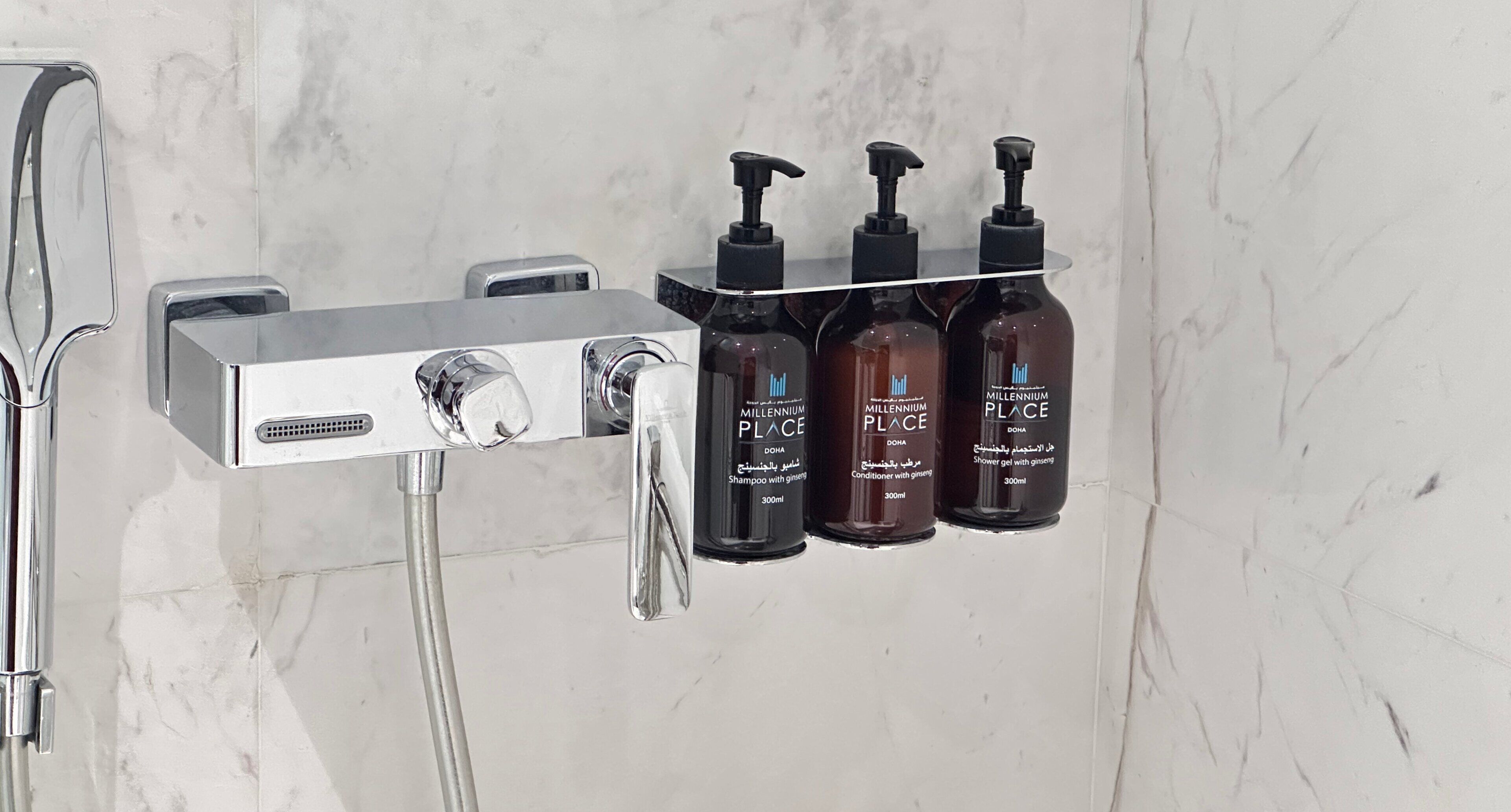 A bathroom with a modern shower system, a handheld showerhead, and three bottles of shampoo and conditioner.