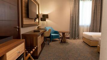 Habitación de hotel con un escritorio de madera, un sillón azul, una mesa redonda, una cama y un espejo grande.