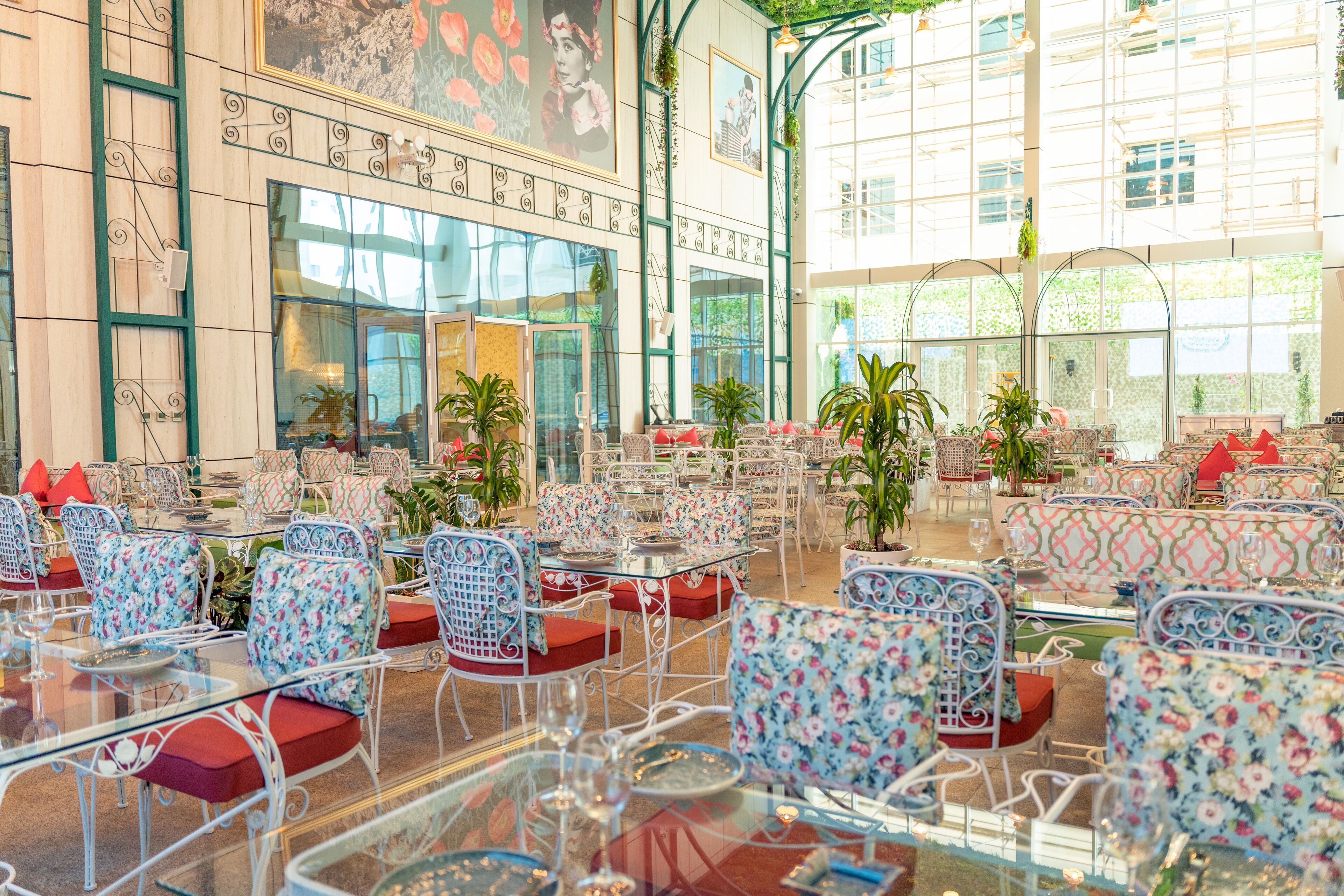 A spacious indoor seating area with glass tables and chairs, large windows, and potted plants.