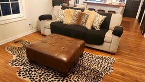 Een woonkamer met een bank, poef en een rug met luipaardprint.