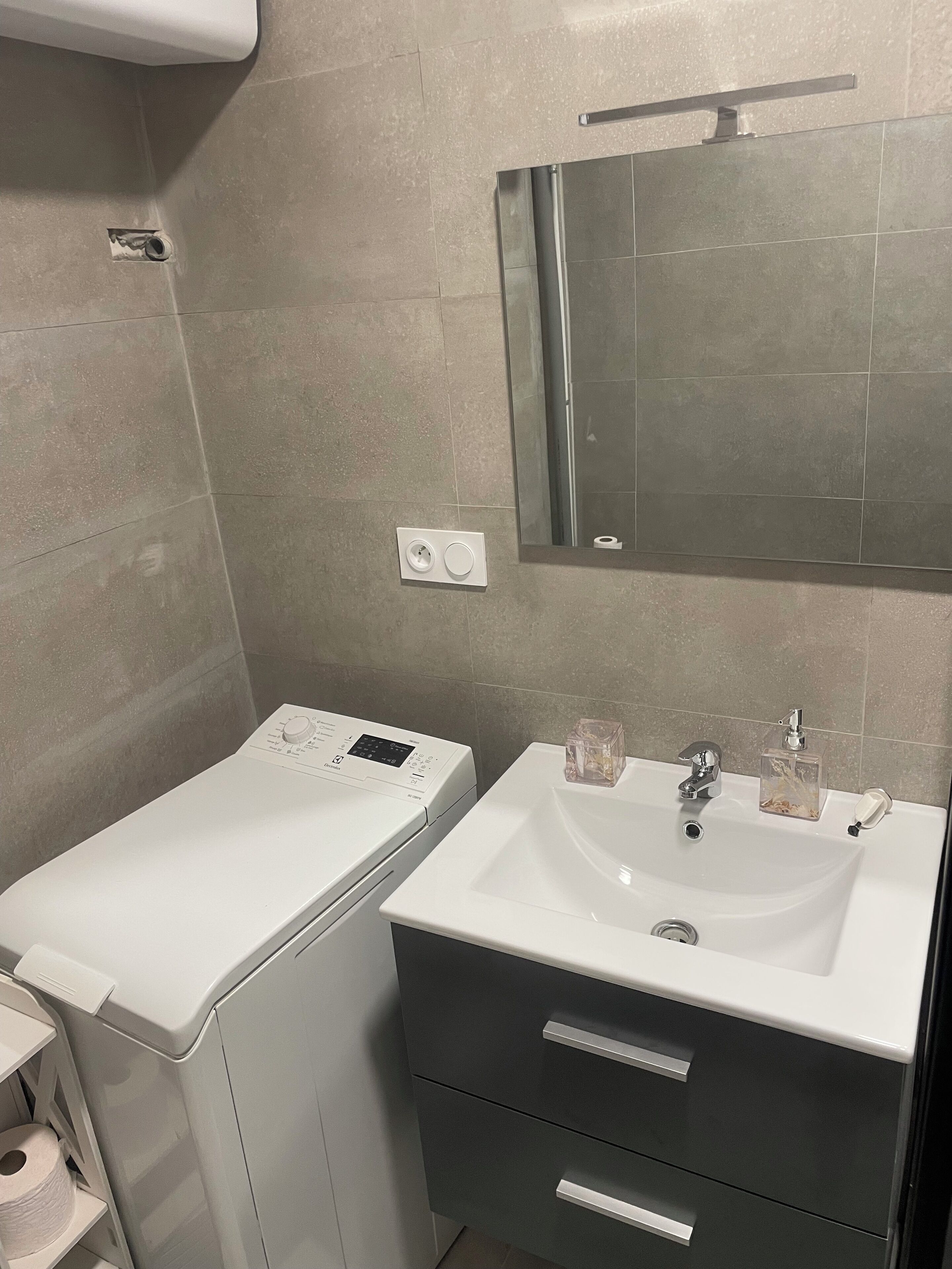 A bathroom with a washing machine, a sink with a mirror, and a toilet.