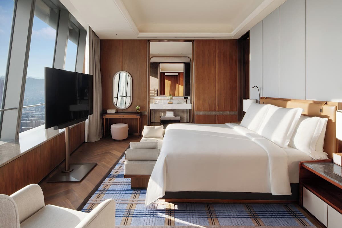 Una habitación de hotel moderna con una cama grande, televisor, baño con espejo y vista a la ciudad.