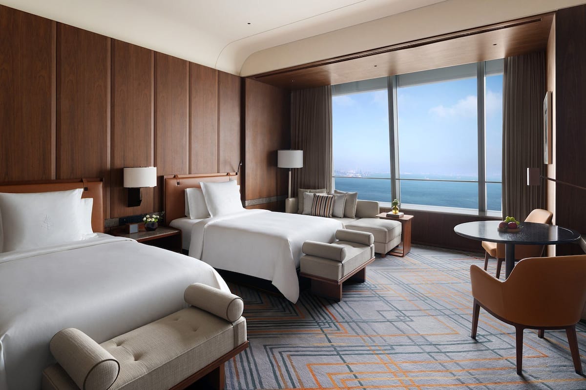 Habitación de hotel con dos camas, un sofá, una mesita y vista al mar.