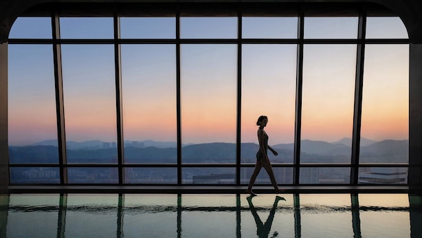 A person walking in a room with a large window overlooking a cityscape at sunset. - Four Seasons Hotel Dalian (Dalian)