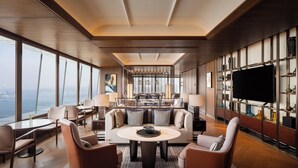 A spacious living room with a large round coffee table, comfortable seating, a television, and a view of the city. - Four Seasons Hotel Dalian (Dalian)