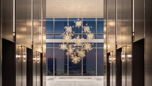 A modern elevator lobby with a reflective floor, glass walls, and a central chandelier. - Four Seasons Hotel Dalian (Dalian)