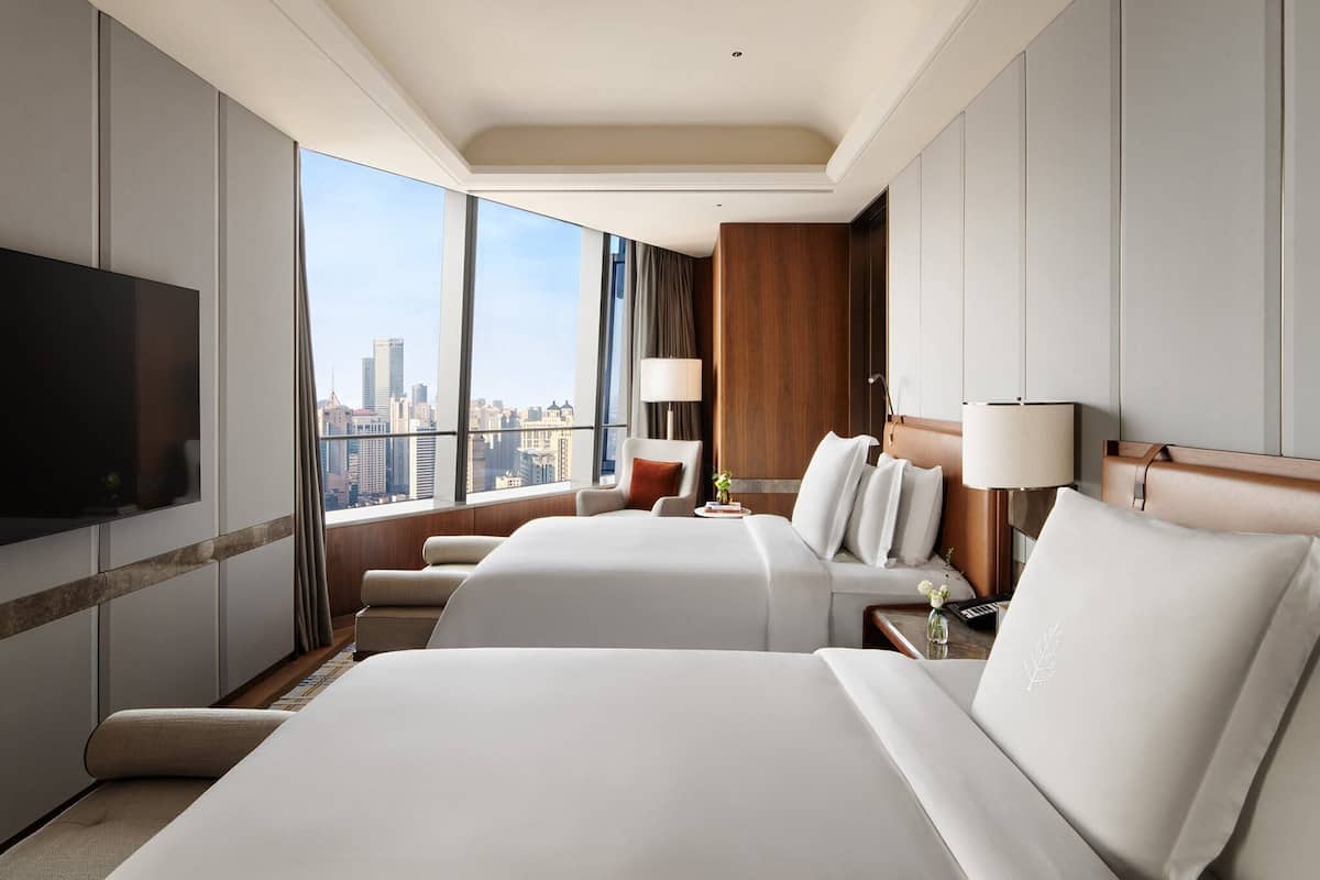 Habitación de hotel con dos camas, televisión, vista a la ciudad y un ventanal grande.