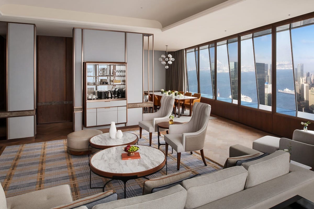 Un moderno vestíbulo de hotel con zona de comedor, amplias ventanas con vistas a la ciudad y una variedad de opciones de asientos, incluyendo sofás y sillones.