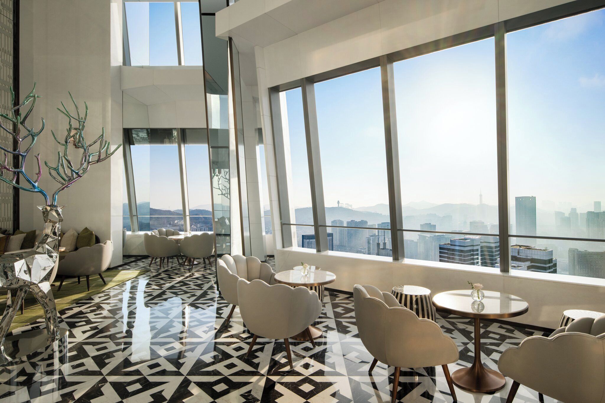 Un salón moderno con un diseño geométrico en el suelo, amplias ventanas con vistas a la ciudad y muebles contemporáneos.