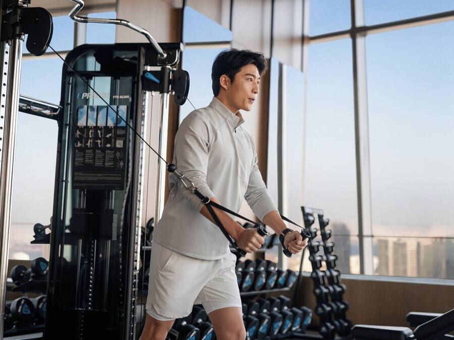 Un gimnasio con equipo de ejercicio y vistas a la ciudad a través de amplias ventanas.