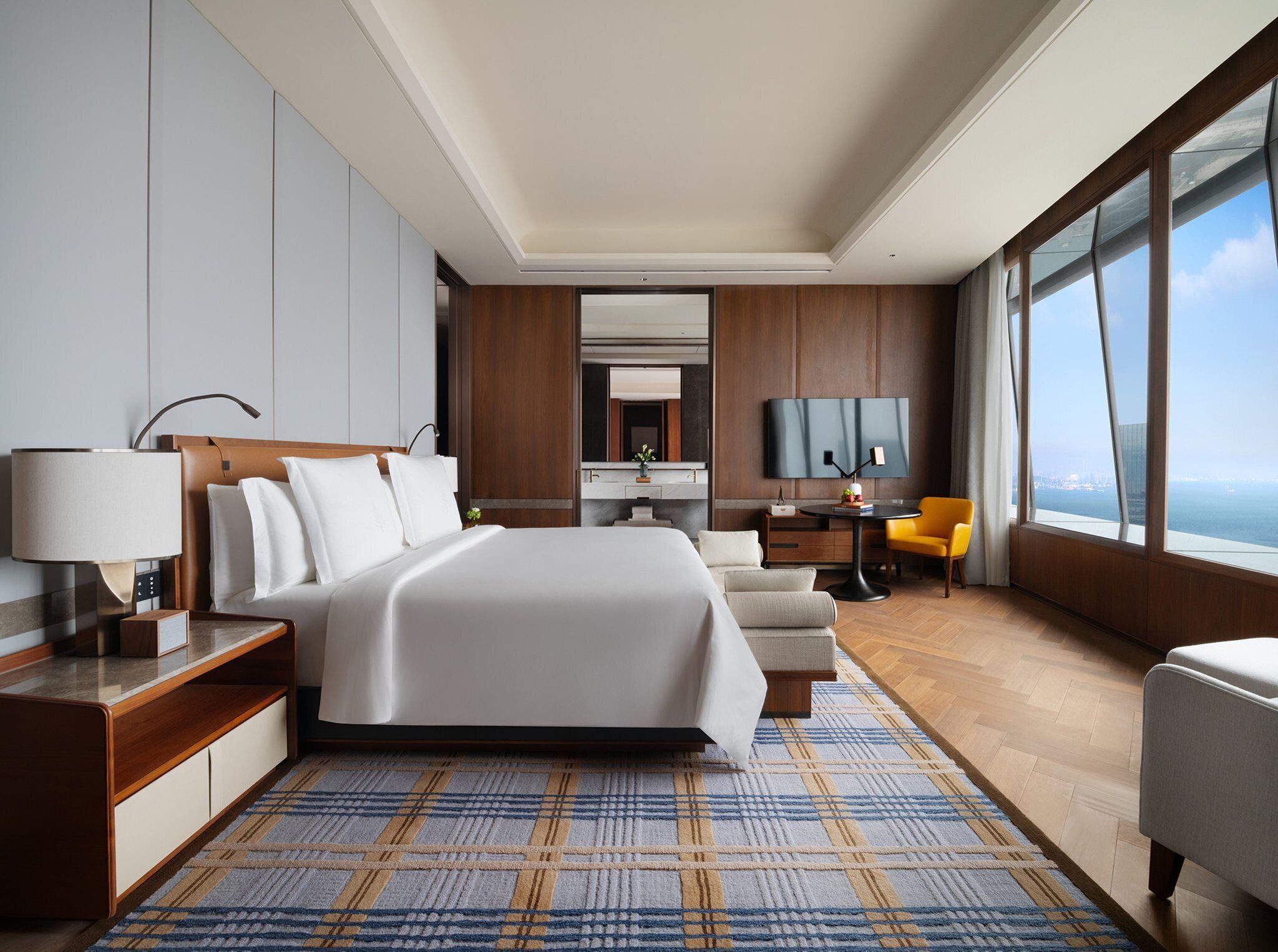 A modern hotel room with a large bed, a desk, a chair, and a TV.