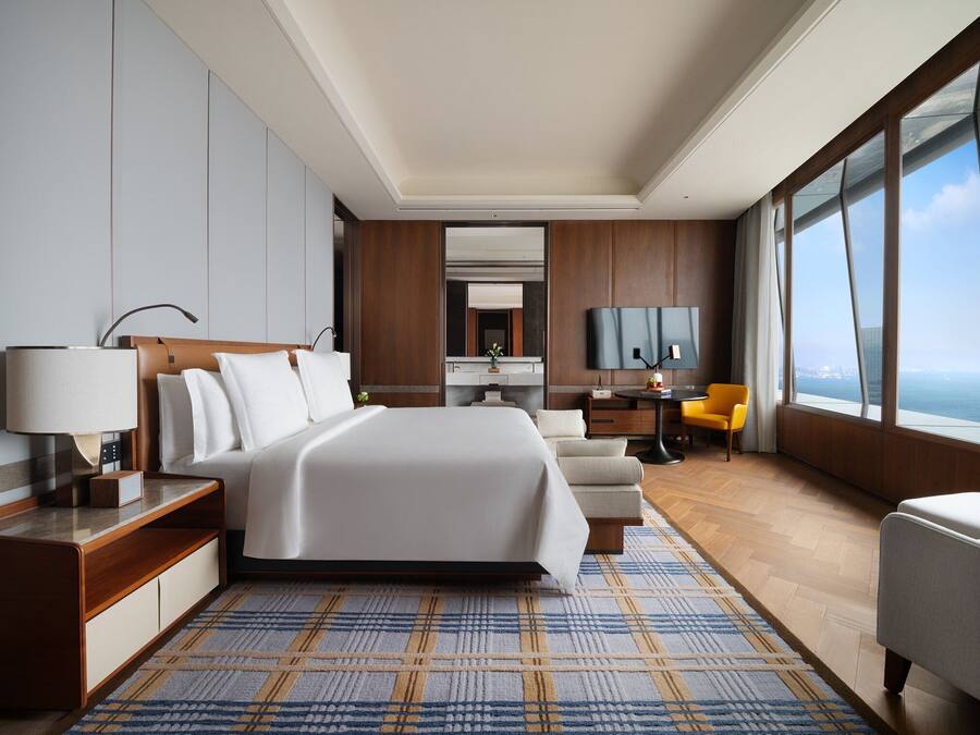 A modern hotel room with a large bed, a desk, a chair, and a TV.
