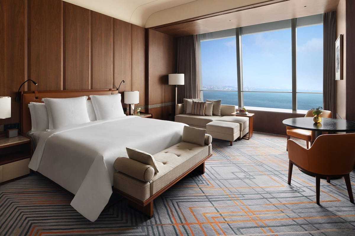 Habitación de hotel con una cama grande, un sofá, una mesa de comedor y vista al mar.