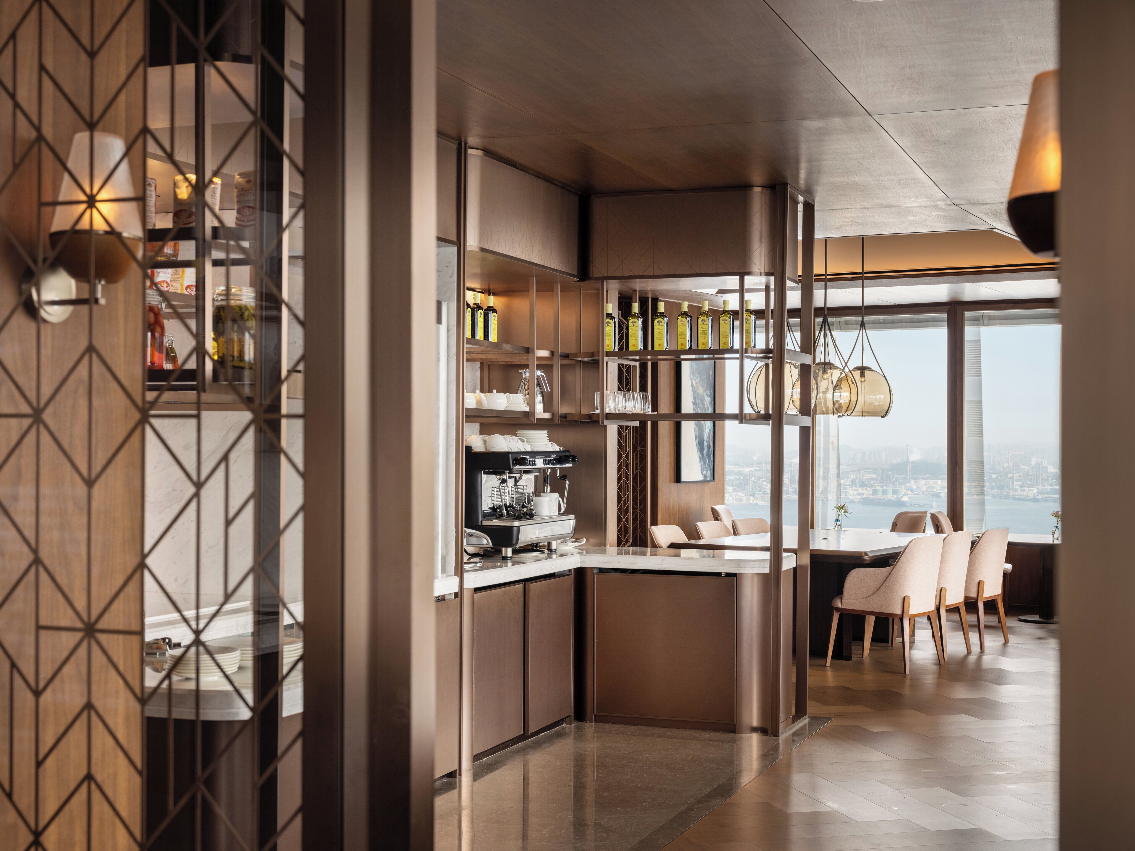 A modern kitchen with a built-in espresso machine, a dining area with a view, and a bar area with bottles.