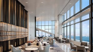 A spacious lounge area with modern furniture, large windows offering a city view, and a decorative bookshelf. - Four Seasons Hotel Dalian (Dalian)