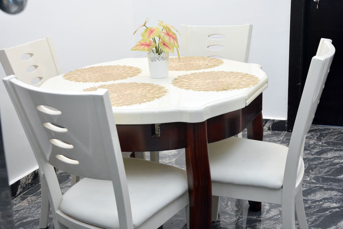 A dining table with a white tablecloth, four woven placemats, and a vase with flowers.