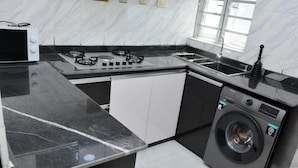 A kitchen with a gas stove, microwave, sink, and a front-loading washing machine. - HABBOT LUXURY APARTMENT  (Ibadan)