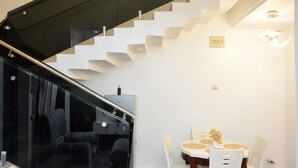 A modern interior with a staircase, a dining area with a table and chairs, and a black sofa. - HABBOT LUXURY APARTMENT  (Ibadan)