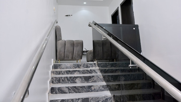 A staircase with marble steps and a handrail, leading to a landing with two grey upholstered chairs. - HABBOT LUXURY APARTMENT  (Ibadan)