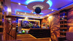 A reception area with a wooden reception desk, a large decorative ceiling, and a wall with a leaf pattern. - The Pelican Beach Resort Mandarmoni (Kanthi)