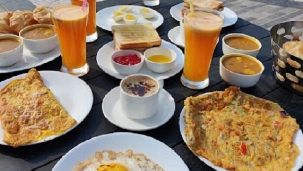 A breakfast spread on a table by a pool with various dishes, drinks, and a view of the pool. - The Pelican Beach Resort Mandarmoni (Kanthi)