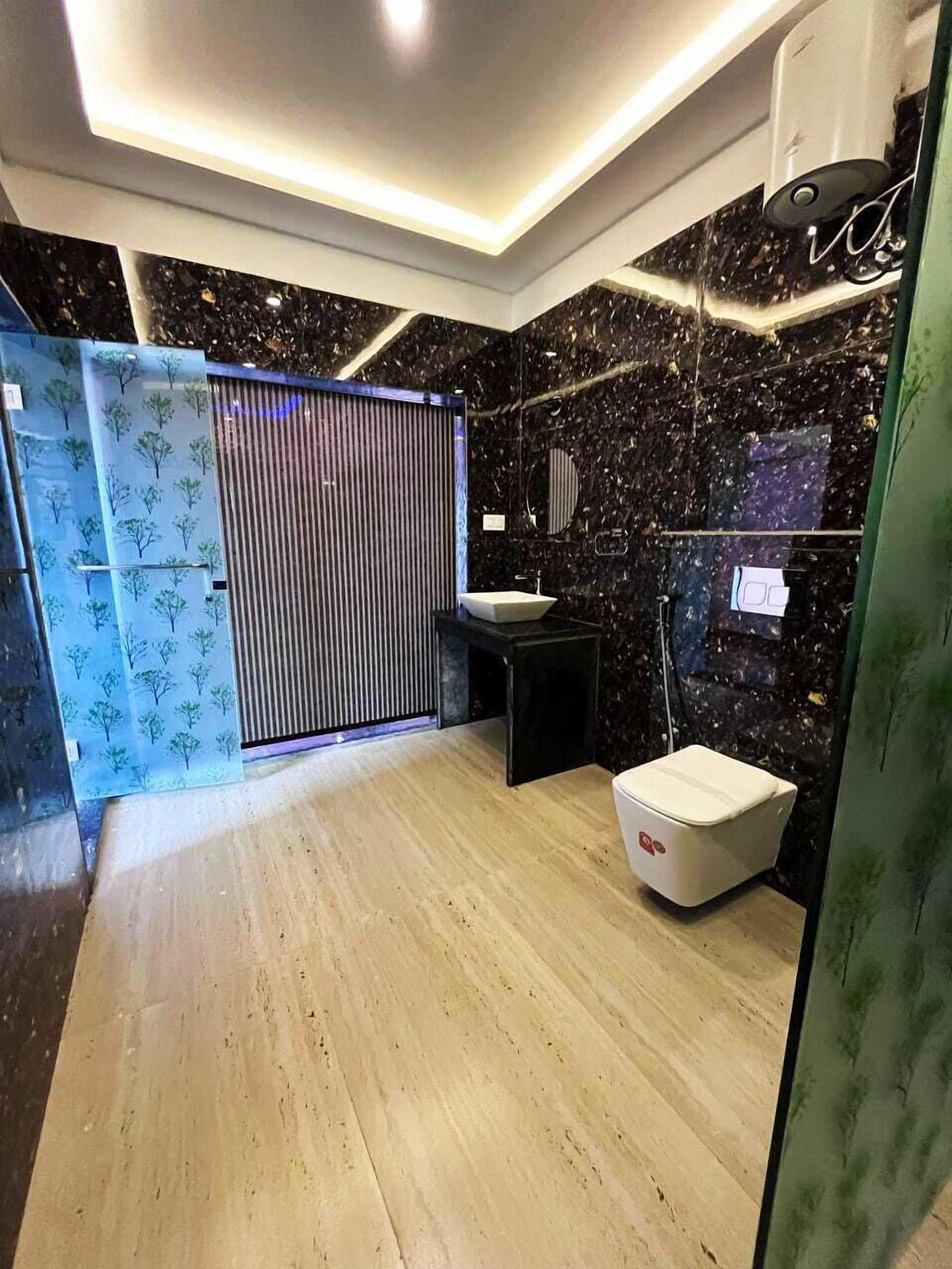 A modern bathroom with a black marble wall, a wooden floor, a white toilet, and a sink with a mirror.