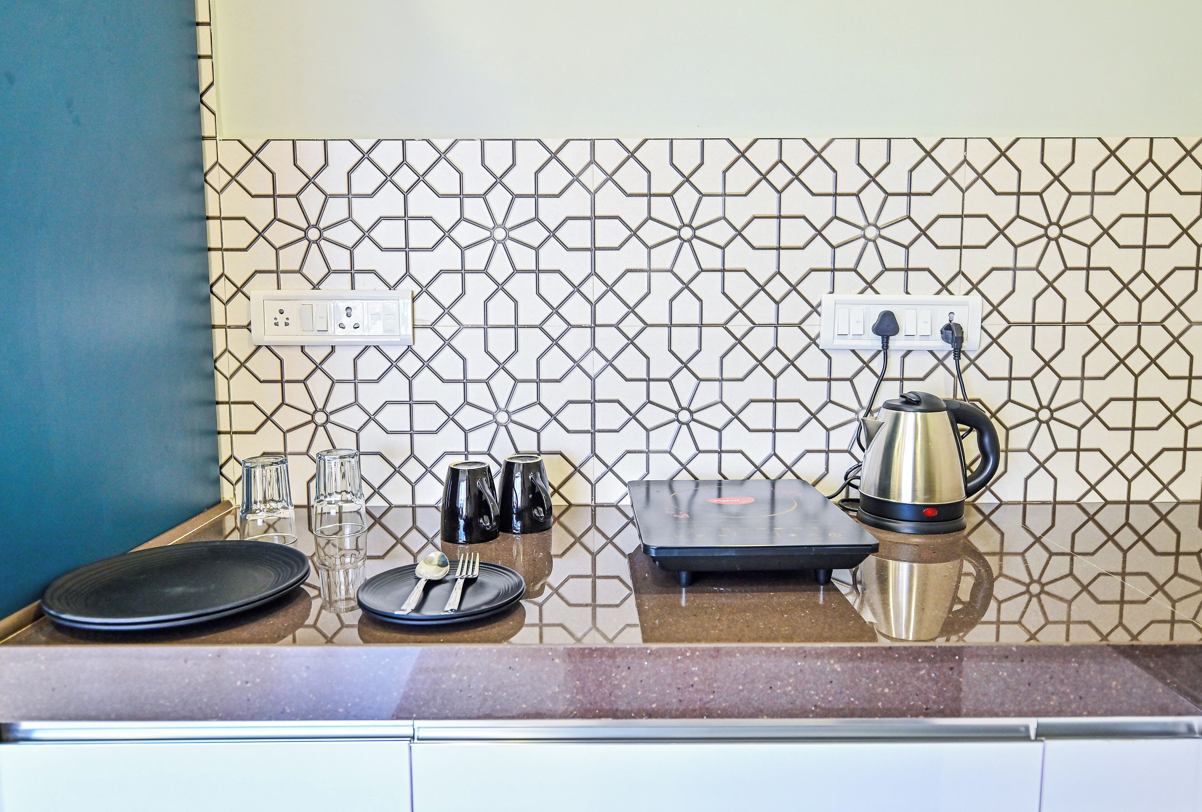 A kitchen counter with a coffee maker, a scale, and a set of glasses and cutlery.