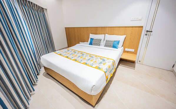 A neatly made bed with a patterned bedspread, a wooden headboard, and a bedside table with a lamp. - Indie Stays Studios (Mumbai)