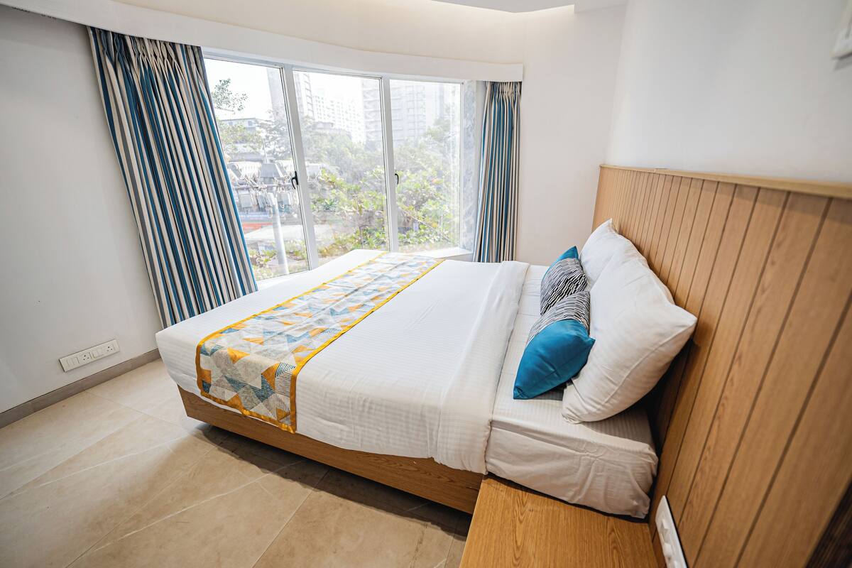 A modern bedroom with a large bed, a wooden headboard, and a view of a cityscape through a large window.