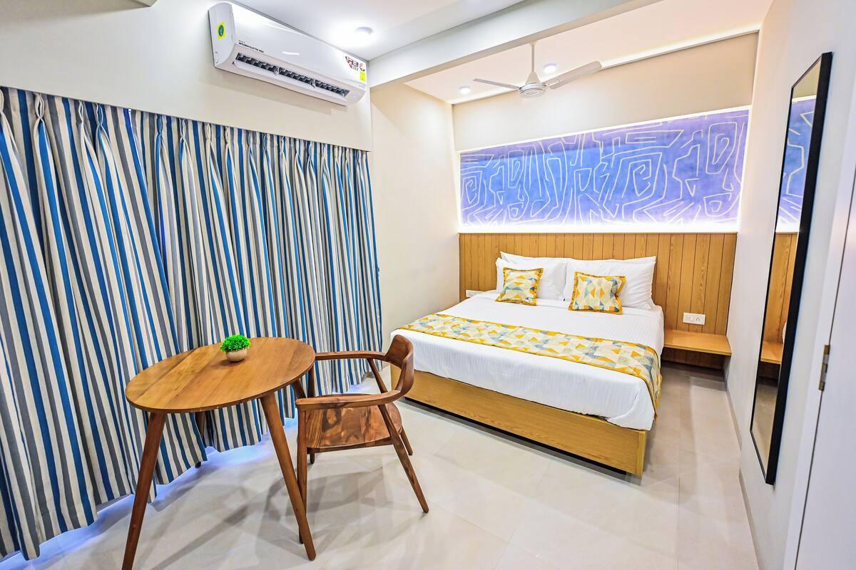 A modern hotel room with a bed, a small wooden table, a chair, and a decorative wall panel.