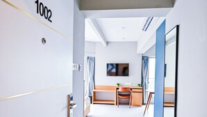 A modern hotel corridor with a number sign "1002" on the wall, a desk with a chair, and a television mounted on the wall. - Indie Stays Studios (Mumbai)