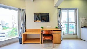 A room with a wooden desk, a chair, a TV on the wall, and a window with curtains. - Indie Stays Studios (Mumbai)