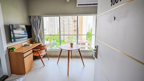 A modern hotel room with a large window, a flat-screen TV, a wooden desk, a small table with a plant, and a wardrobe with the number 1001. - Indie Stays Studios (Mumbai)